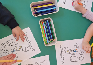 Dzieci przy stoliku kolorują dwie różne skarpetki.
