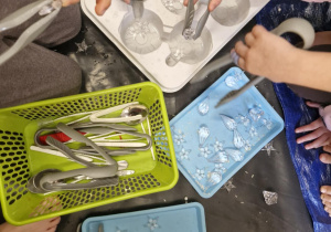 Dzieci za pomocą plastikowych szczypiec wyławiają z pojemnika z wodą i lodem diamenty.