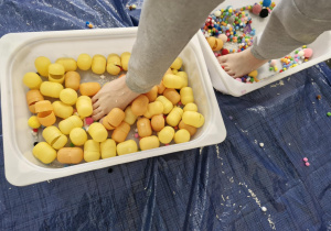 Dzieci przechodzą przez pojemniki z kolorowymi pomponikami i jajkami z kinder niespodzianek.
