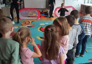 Dzieci stoją w kolejce do kopnięcia piłki. Przed nimi stoją trenerzy.