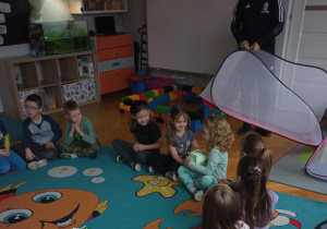 Dzieci siedzą w kole i podają sobie piłkę.