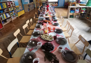 Długi wigilijny stół, na którym znajdują się talerze z uszkami, pierogi, ryba, mandarynki