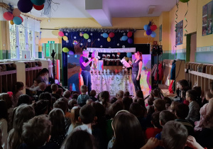 Na scenie mężczyzna z lalką i kobieta z kózką. Dzieci oglądają przedstawienie teatralne.