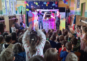 Na scenie mężczyzna i kobieta śpiewają piosenkę. Dzieci klaszczą w rytm muzyki.
