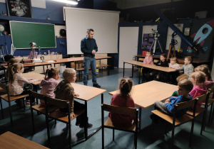 Dzieci siedzą przy stolikach i słuchają o gwiazdach.