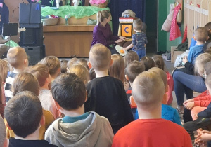 Kobieta i chłopiec stoją przed siedzącą figurą robota. Dzieci patrzą na scenę.