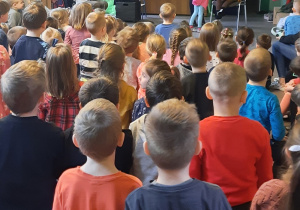 Kobieta i dziewczynka stoją przed siedzącą figurą robota. Dzieci patrzą na scenę.