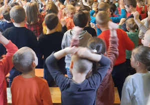 Kobieta i dwie dziewczynki tańczą na scenie z pomponami. Dzieci powtarzają za nimi ruchy.