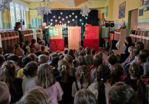 Dzieci oglądają przedstawienie teatralne. Na scenie aktorzy z lalkami teatralnymi.