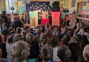 Dzieci oglądają przedstawienie teatralne. Na scenie aktorzy z lalkami teatralnymi.