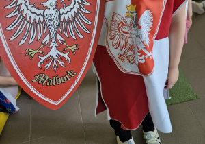 Chłopiec w stroju trzyma godło Polski na pokazie mody patriotycznej.