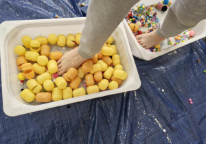 Dzieci przechodzą przez pojemniki z kolorowymi pomponikami i jajkami z kinder niespodzianek.