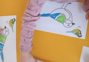 Dzieci pracują przy stoliku - kolorują pastelami ptaki.
