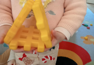 Dziewczynka trzyma w rączkach karmnik ułożony z klocków.