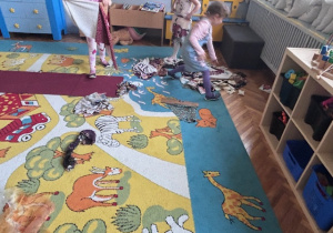 Dziewczynki podczas wybierania materiałów na stroje, na dywanie rozrzucone materiały.