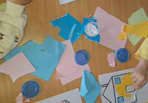 Dzieci starannie przyklejają fragmenty papieru do kartki.