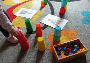 Dziewczynka wybiera kolor kubeczka potrzebny do ułożenia wieży według instrukcji.
