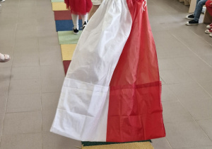 Dzieci na wybiegu - dziewczynki w biało-czerwonych strojach i chłopiec z zawieszoną na plecach biało-czerwoną flagą.