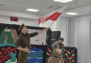 Na scenie żołnierz z flagą Polski, kobieta - żołnierz oraz Miś Wojtek.