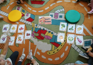 Na dywanie leżą obrazki podzielone na dwie grupy: warzywa i owoce.