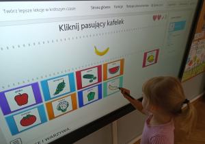Dziewczynka wykonuje zadanie na tablicy multimedialnej – klika w obrazek banana.