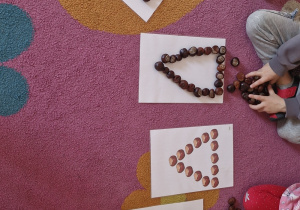 Dzieci układają różne wzory z kasztanów.