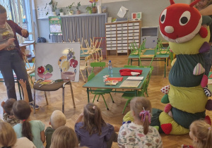 Jedna kobieta trzyma stonogę, a druga przyczepia na tablicy owoce i warzywa.