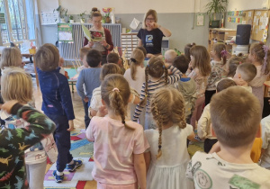 Dzieci słuchają fragmentów opowiadań czytanych przez kobietę.