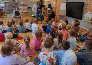 Dzieci siedzą na dywanie i słuchają czytanej przez autorkę książkę "Stonoga Jadzia"