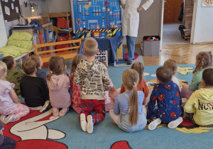 Dzieci patrzą na kobietę w fartuszku, która w ręce trzyma maskotkę - kota.