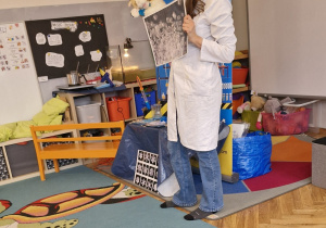 Kobieta w fartuszku w jednej ręce trzyma maskotkę - kota, a w drugiej ilustracje przedstawiającą cukier w dużym przybliżeniu.