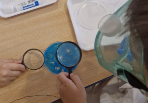 Dzieci z wykorzystaniem lupy obserwują różne materiały.