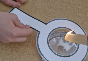 Chłopiec trzyma wycięty i zalaminowany klucz. Nad kluczem nauczycielem trzyma zapaloną świeczkę.