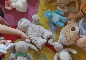 Dzieci trzymają swoje pluszowe misie na dywanie.