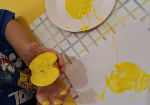 Dzieci stempluje jabłkiem zamoczonym w żółtej farbie na kartce.