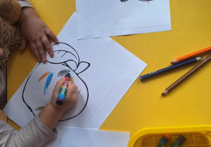 Dzieci kolorują kredkami szablony owoców.