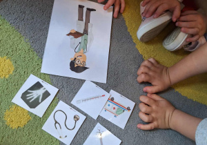 Na dywanie wokół dzieci ilustracja przedstawiająca zawód lekarza oraz jego atrybuty.