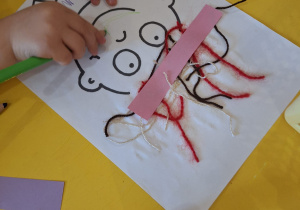 Dziecko koloruje kredkami swoją pracę - kontur twarzy.