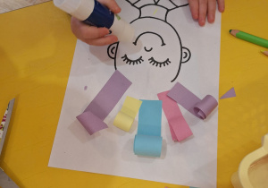 Dziecko klejem smaruje swoją pracę, aby przykleić kolorowe włosy.