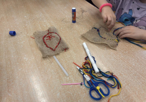 Dzieci przy stoliku wyszywają włóczką liście. Na stole nożyczki, plastikowe igły i włóczki.