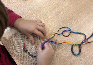 Dziecko wyszywa kolorową włóczką kształt liścia.