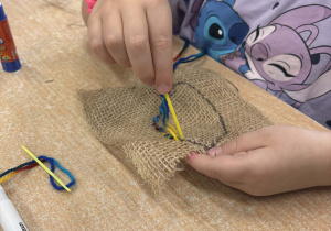 Dziecko z wykorzystaniem włóczki wyszywa kształt liścia.