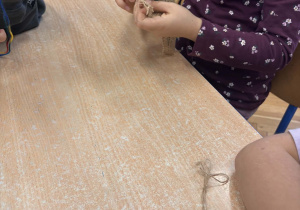 Dzieci pracują przy stoliku - z wykorzystaniem kolorowej włóczki wyszywają kształt liścia.