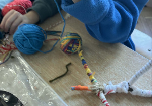 Dzieci przy stoliku owijają patyki kolorowymi włóczkami.