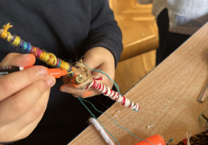 Dzieci tworzą ludziki z patyków, owijając je kolorową włóczką.