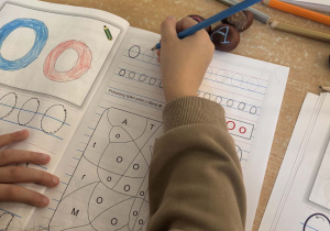 Dziecko uzupełnia książkę , pisze literę "O" po śladzie.