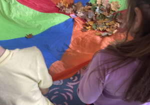 Dzieci trzymają chustę animacyjna, na środku chusty leżą liście.