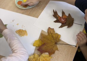 Dzieci przy stoliku odbijają farbami jesienne liście.
