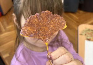 Dziewczynka trzyma przed twarzą pomalowany liść miłorzębu.