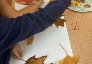 Dzieci przy stoliku odbijają liście przy użyciu farb.